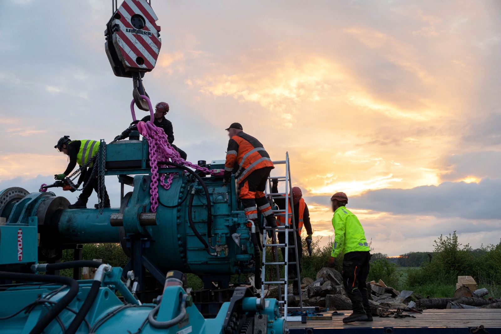Eine Crew schlägt bei Sonnenuntergang eine Großkomponente am Kranhaken an.